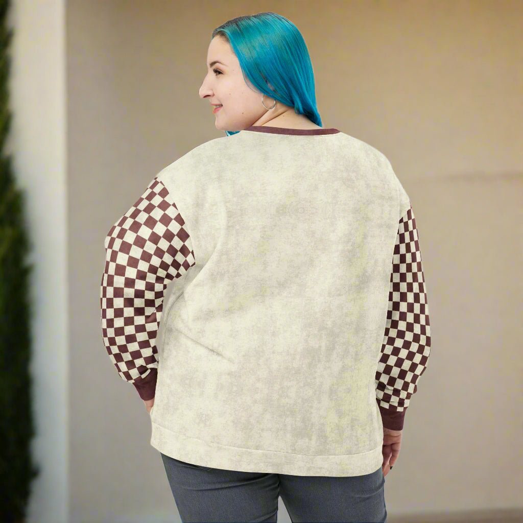 Person wearing a beige sweatshirt with checkered sleeves against a plain background