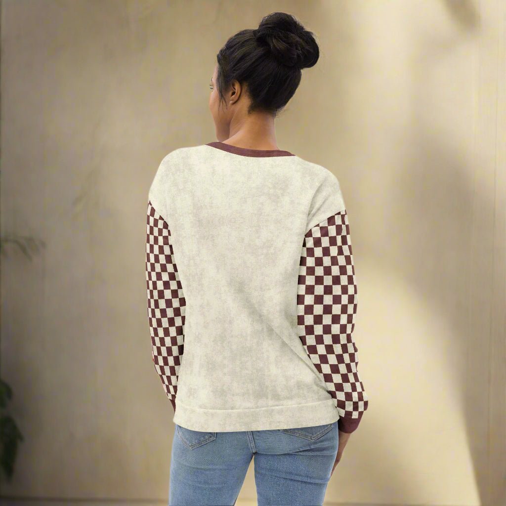 Person wearing a cream sweater with checkered sleeves on a beige background
