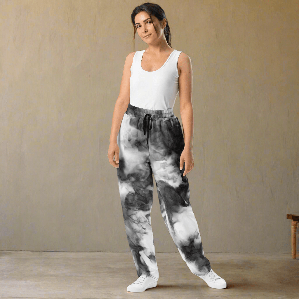 Woman wearing tie-dye pants and a white tank top on a neutral background