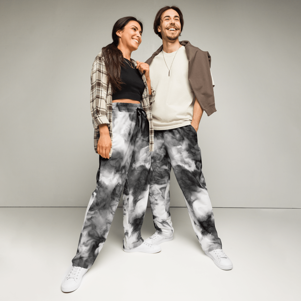 Two people wearing tie-dye pants standing against a plain background