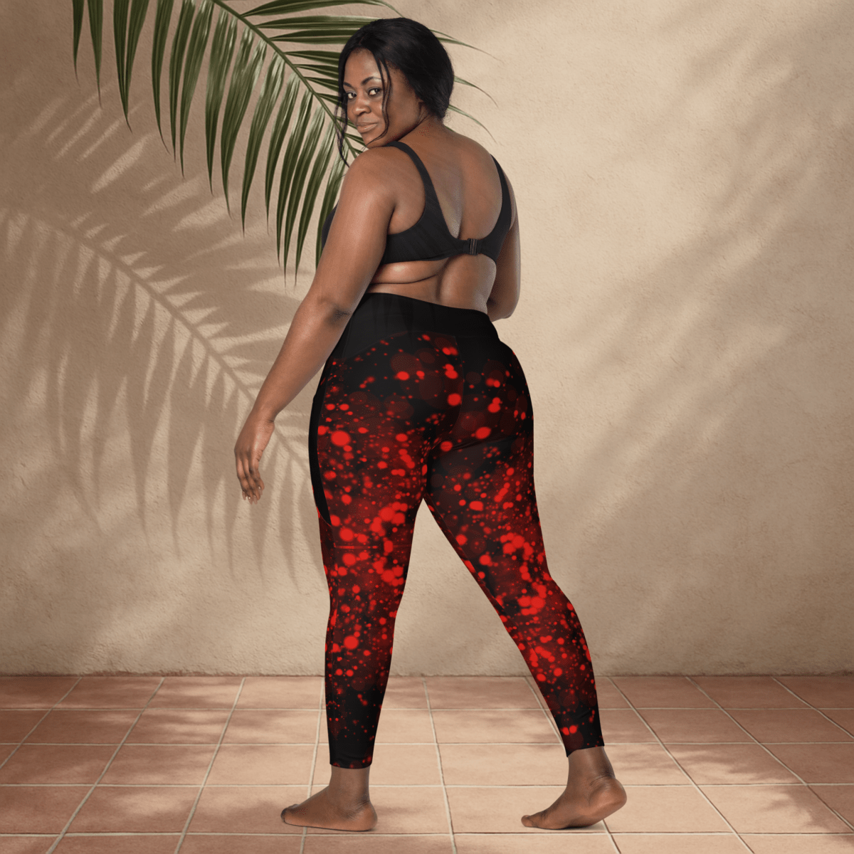 Woman wearing black and red patterned leggings standing against a beige wall.