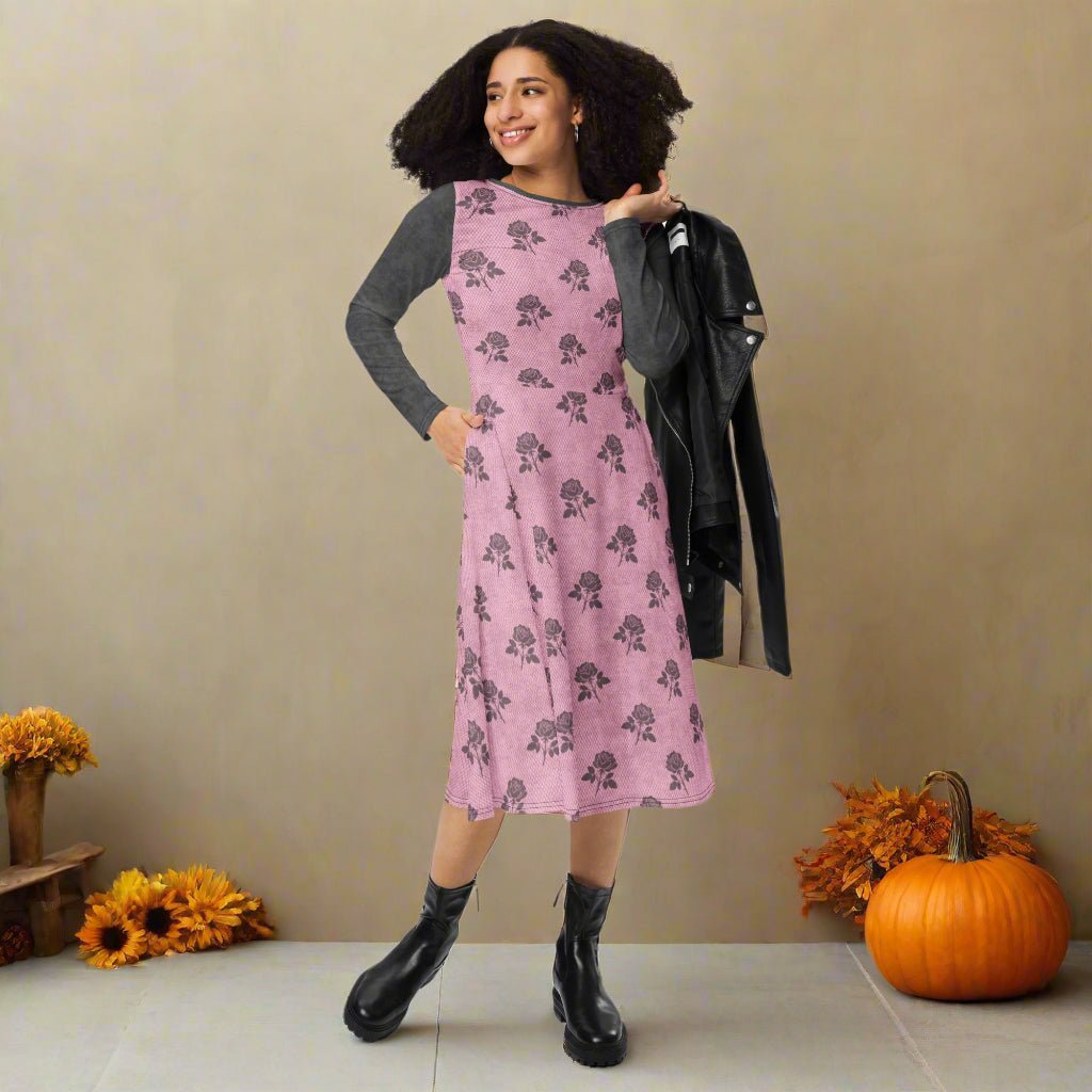 Woman wearing a pink floral dress with a gray long-sleeve shirt underneath, standing against a fall background.