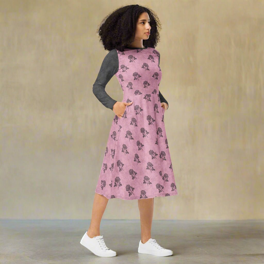 Woman wearing a pink floral dress with a gray long-sleeve shirt underneath on a neutral background