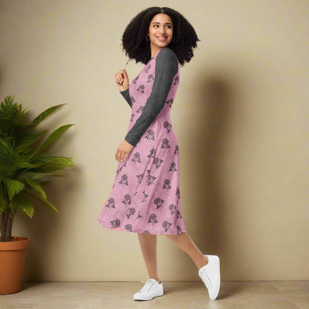 Woman wearing a pink floral dress with a gray long-sleeves, standing against a beige wall.