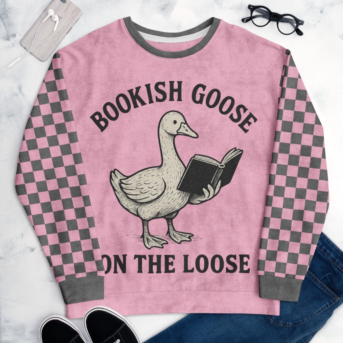 Pink sweater with a goose holding a book design and text 'Bookish Goose on the Loose' on a marble surface.