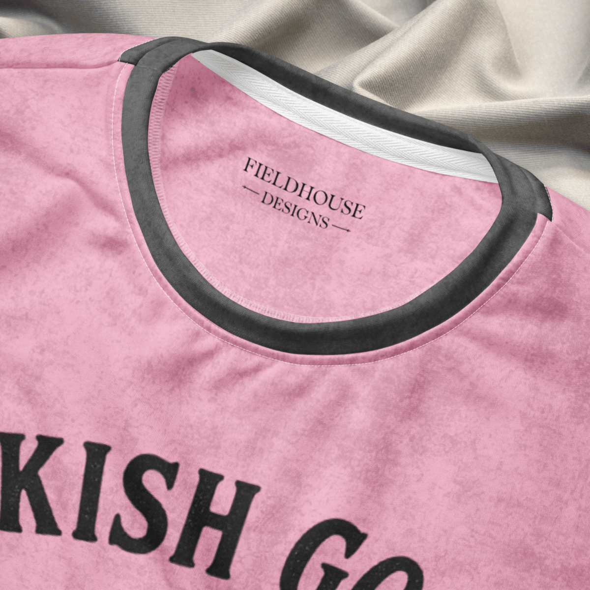 Pink shirt with black text and neckline trim on a textured fabric background