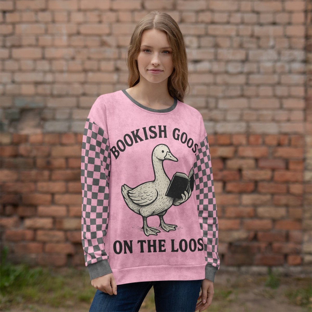 Person wearing a pink sweater with a goose graphic and text in front of a brick wall