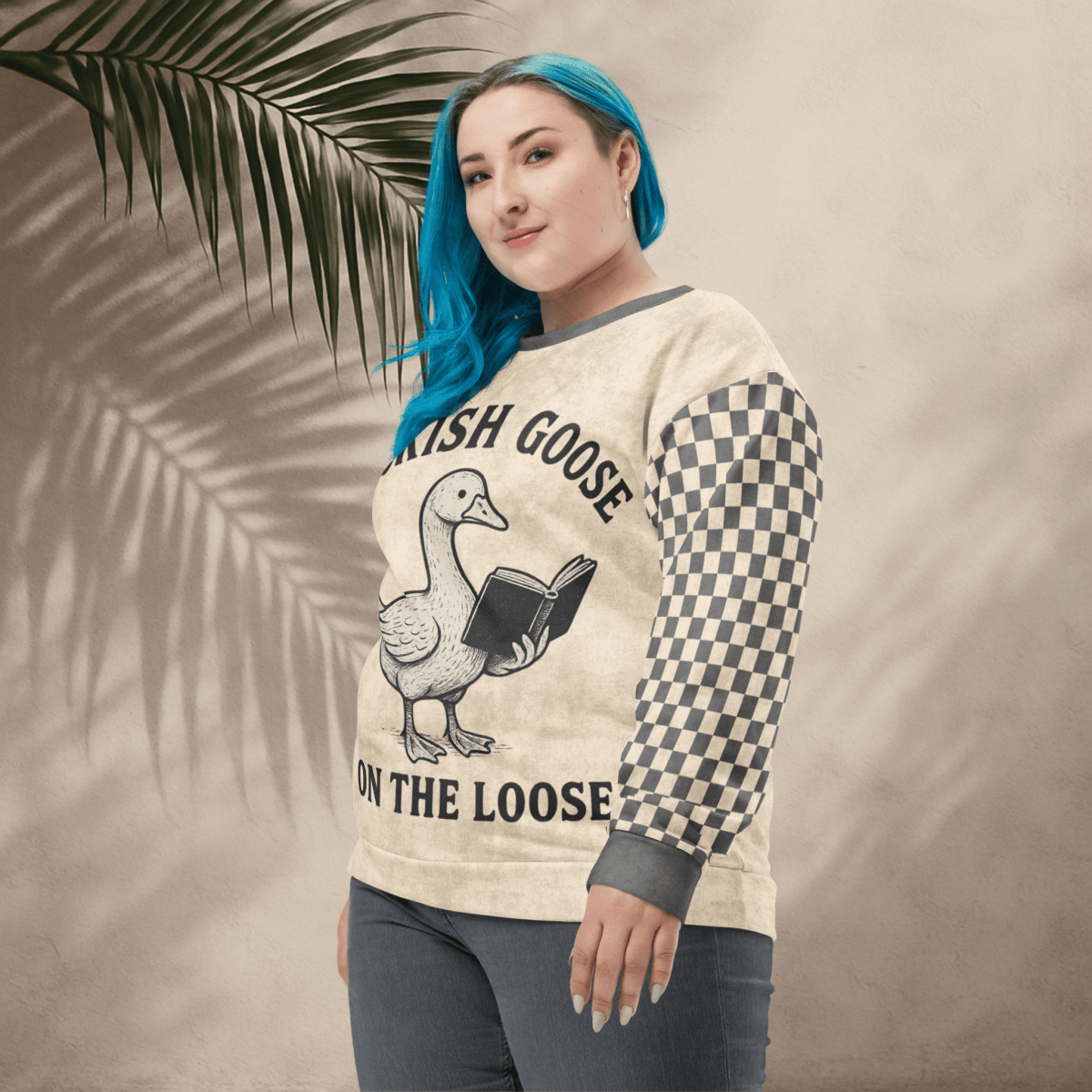 Person wearing a sweater with a goose graphic and text, standing against a neutral background with a leaf.