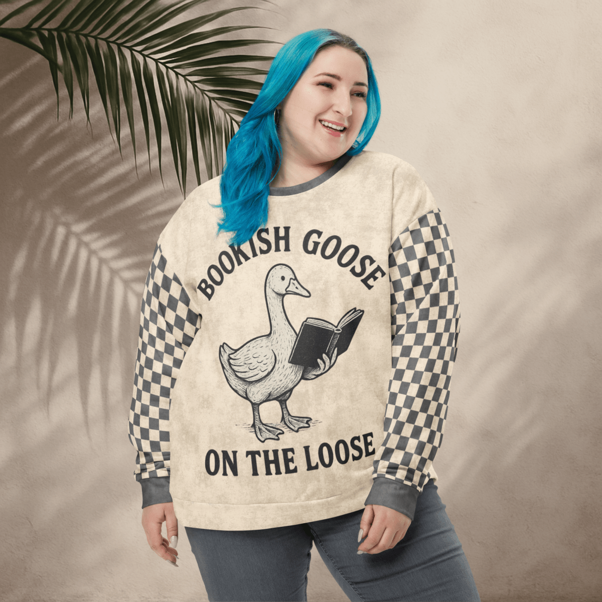 Person wearing a sweater with a goose graphic and text, standing against a beige wall with a leafy branch.