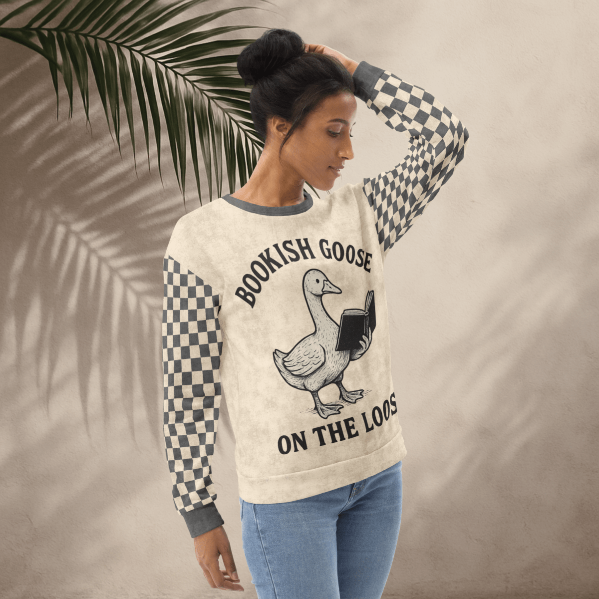 Woman wearing a sweater with a graphic and text, standing against a neutral background with a leaf.