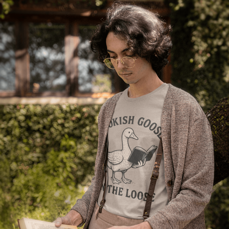 Person wearing a graphic t-shirt with a goose design, reading a book outdoors.