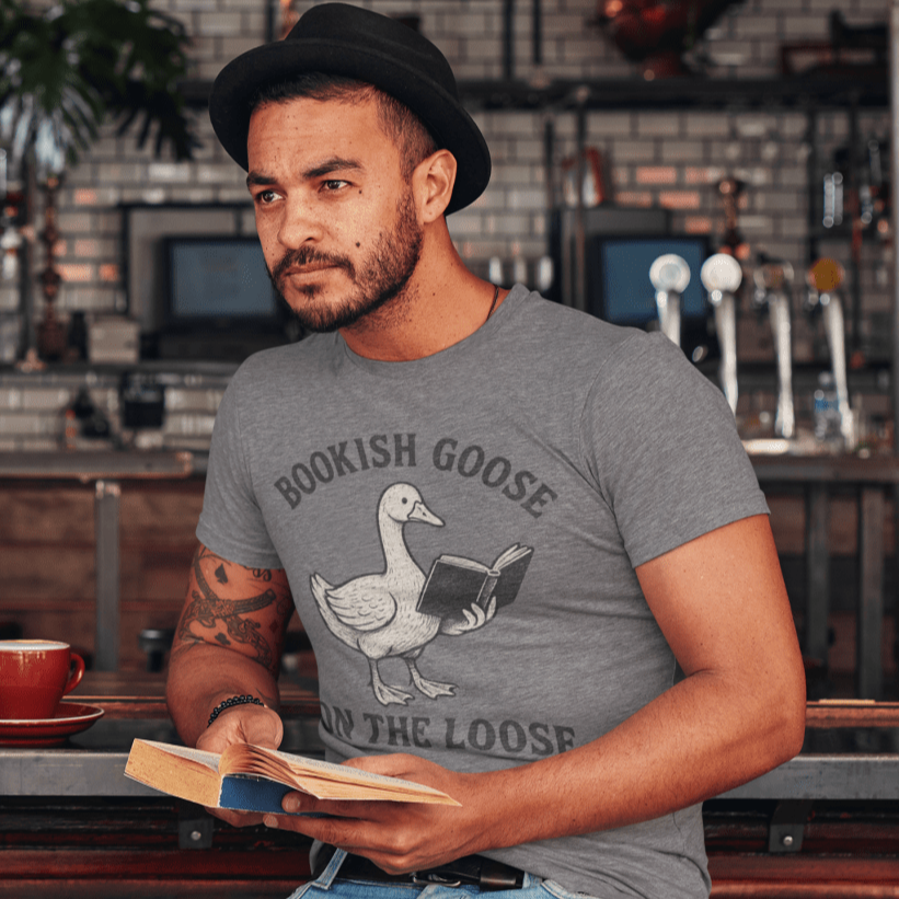Man wearing a gray t-shirt with a graphic design, sitting at a bar holding a book.
