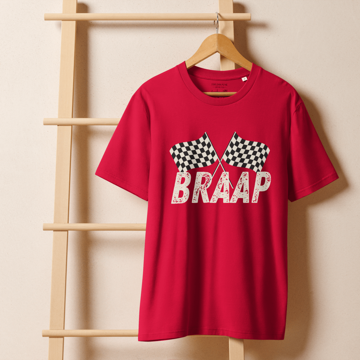 Red t-shirt with 'BRAAP' and checkered flags design on a wooden hanger against a beige wall.