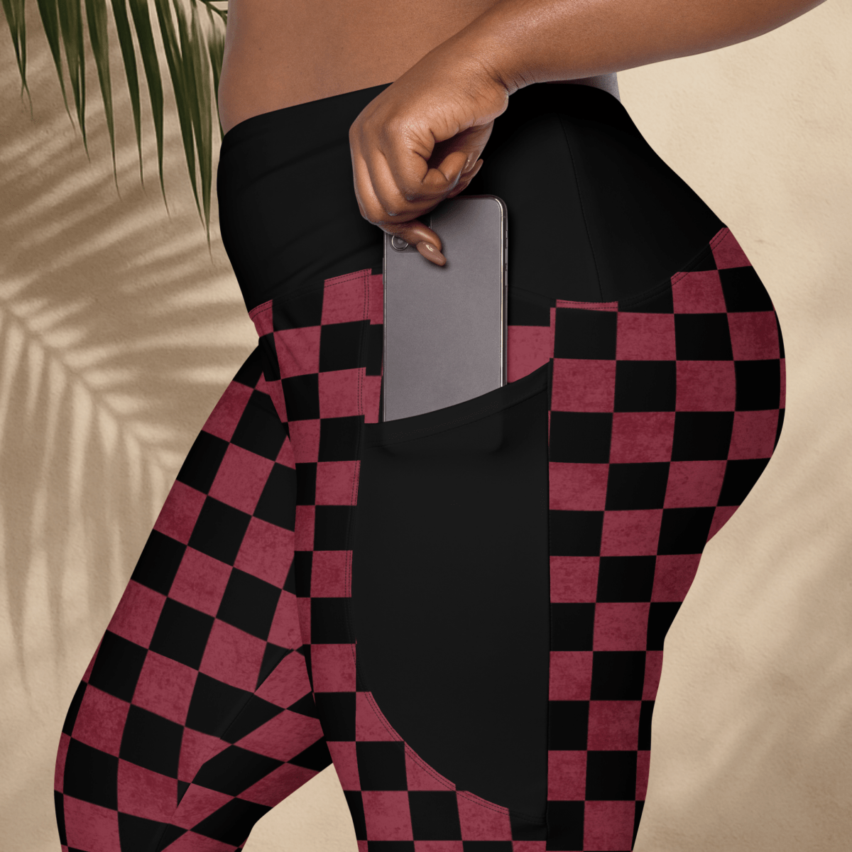 Person wearing black and burgundy checkered leggings with a pocket holding a phone.