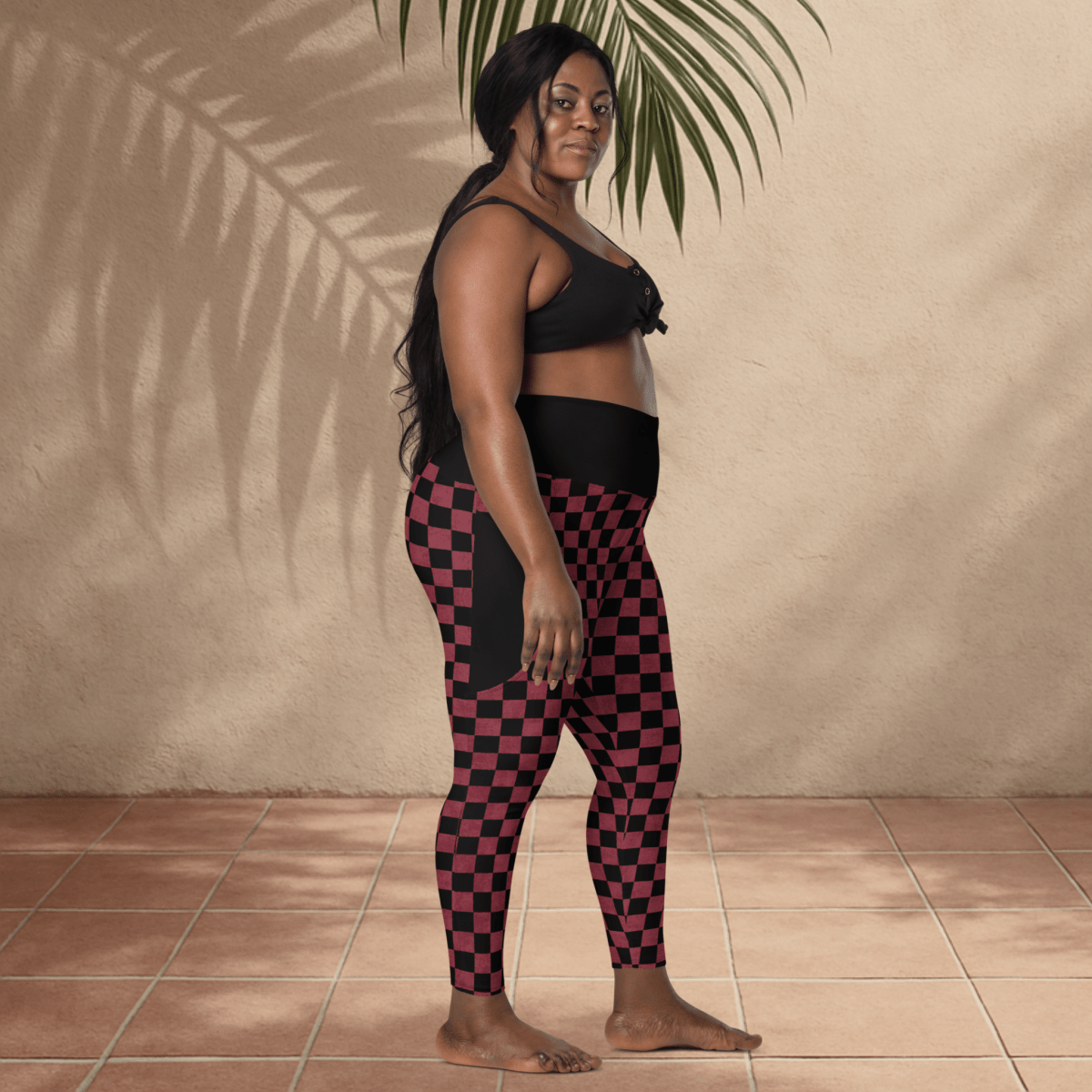 Woman wearing black and burgundy checkered leggings against a beige wall.