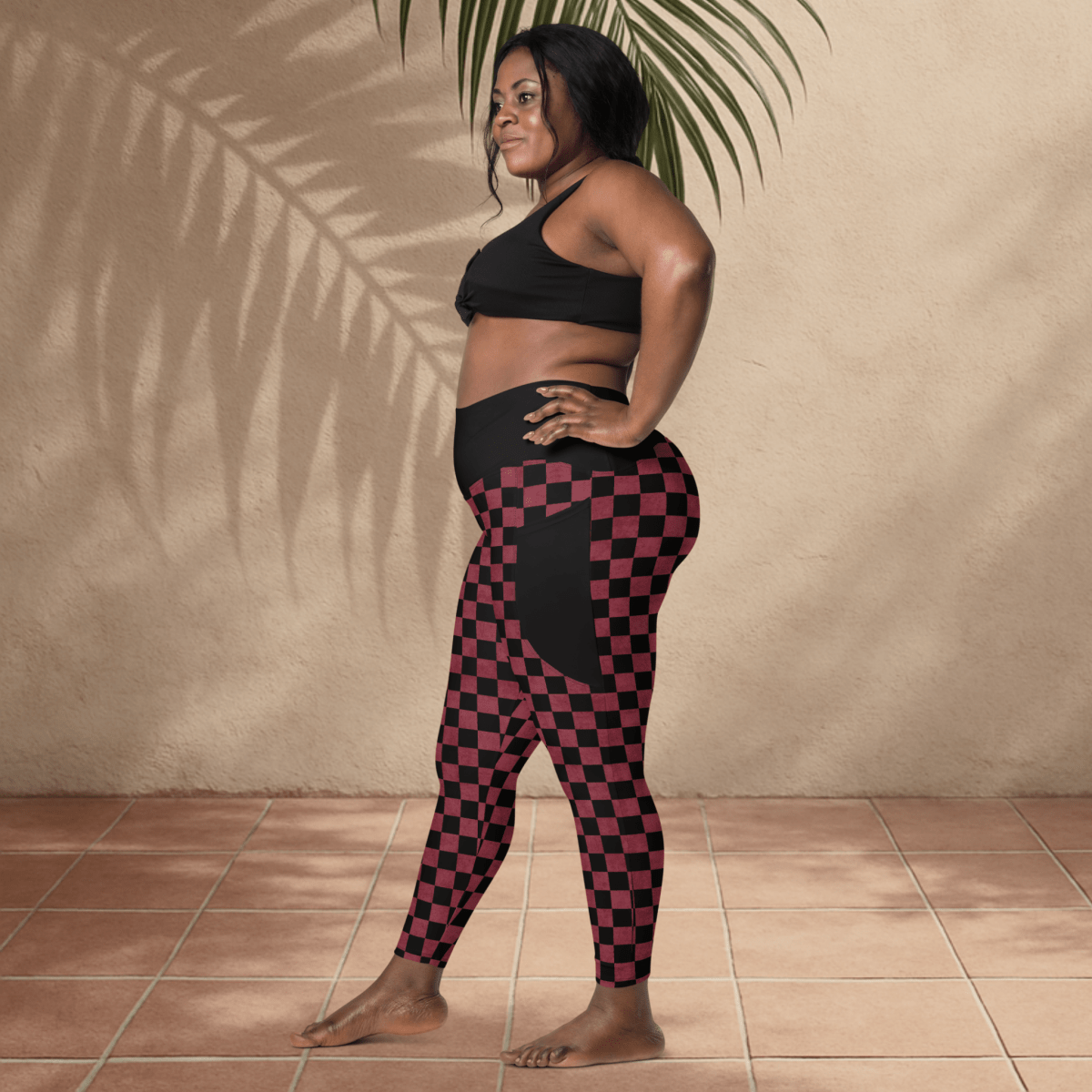 Woman wearing a black sports bra and checkered leggings standing against a beige wall.