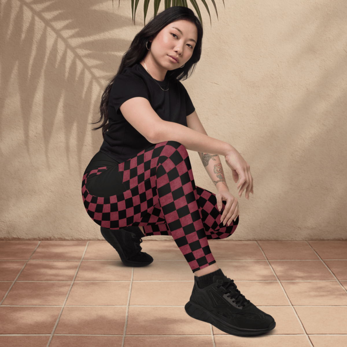 Person wearing a black t-shirt and burgundy checkered pants sitting on the floor with a leaf above them against a beige wall.