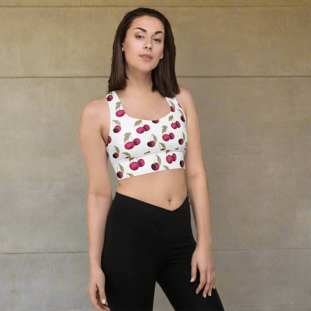Woman wearing a sports bra with cherry pattern and black leggings on a beige background
