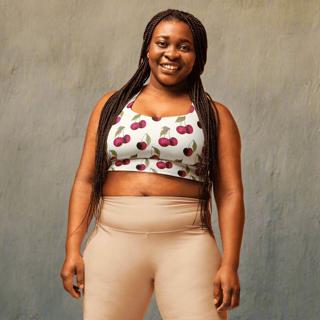 Woman wearing a white sports bra with cherry pattern and beige pants on a beige background