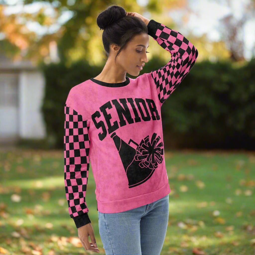 Person wearing a pink sweatshirt with 'Senior' and cheerleading graphic outdoors