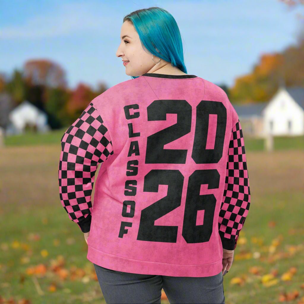 Person wearing a pink sweatshirt with 'Class of 2026' text and checkered sleeves outdoors