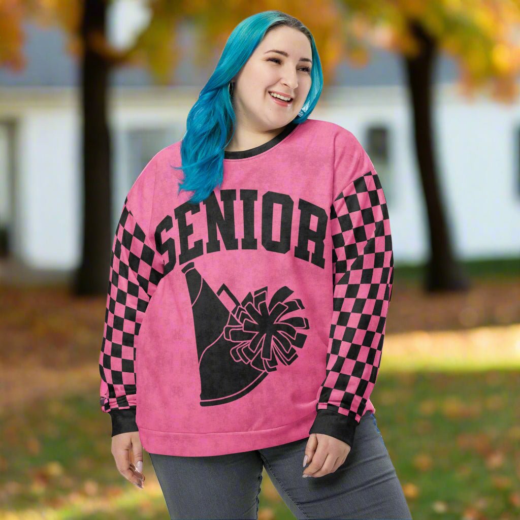 Person wearing a pink Cheerleading 'Senior' sweatshirt with black and pink checkered sleeves outdoors