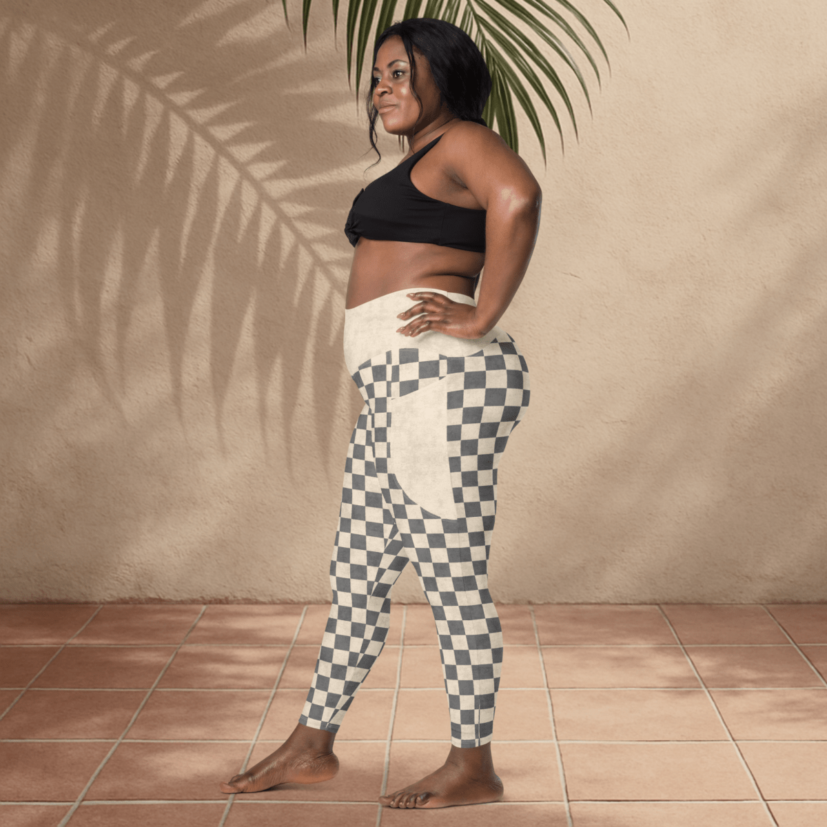 Woman wearing a black sports bra and checkered leggings standing against a beige wall.