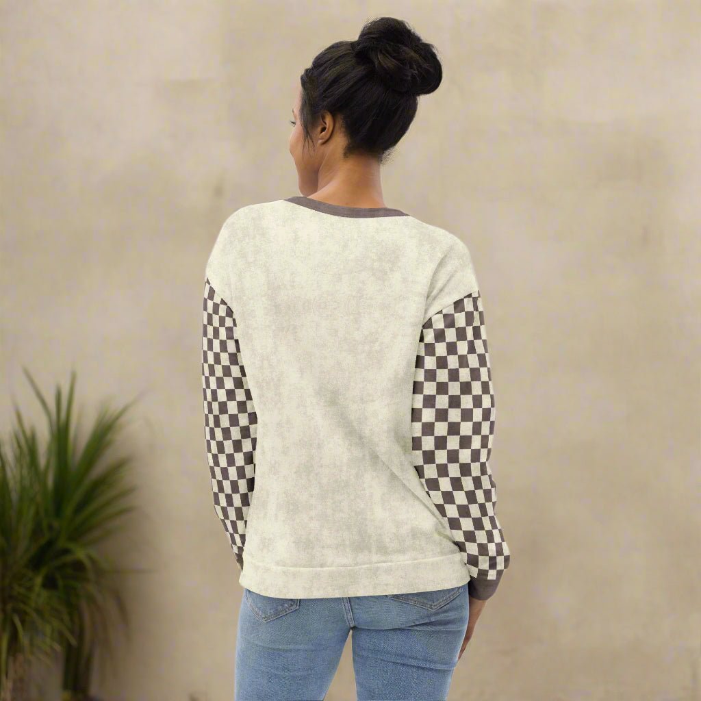 Person wearing a cream sweater with checkered sleeves on a neutral background