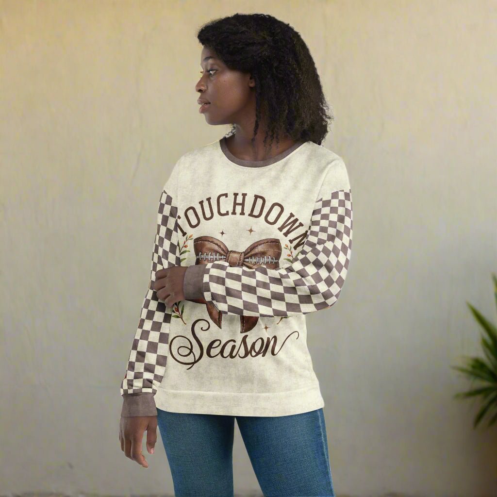 Woman wearing a long-sleeve shirt with 'Touchdown Season' text and checkered sleeves on a neutral background
