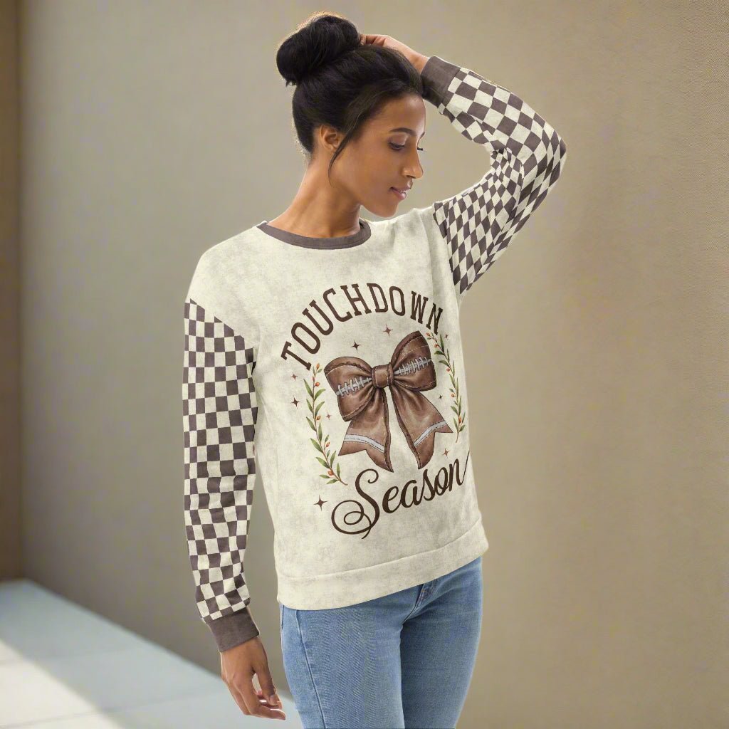 Woman wearing a sweater with 'Touchdown Season' text and checkered sleeves against a plain background