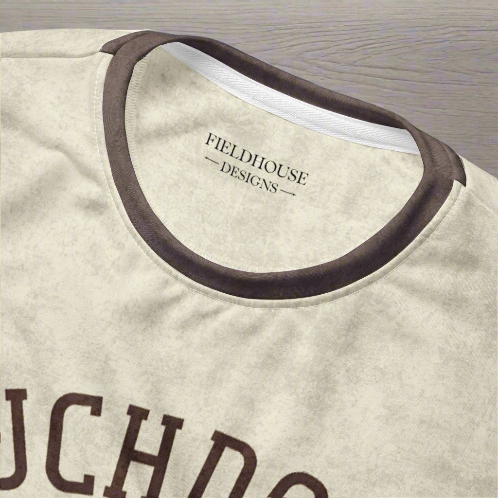 Close-up of a beige shirt with brown trim and 'Fieldhouse Designs' branding.
