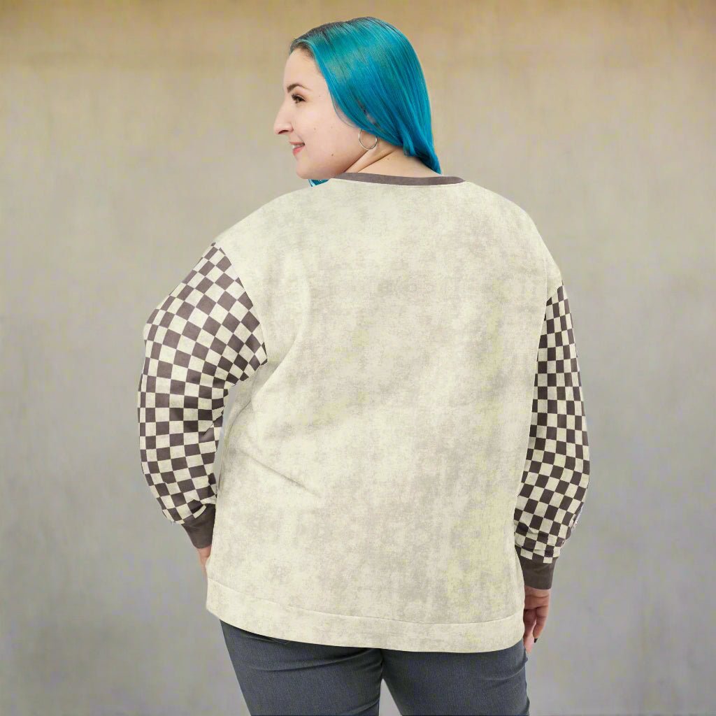 Person wearing a light-colored sweater with checkered sleeves against a plain background