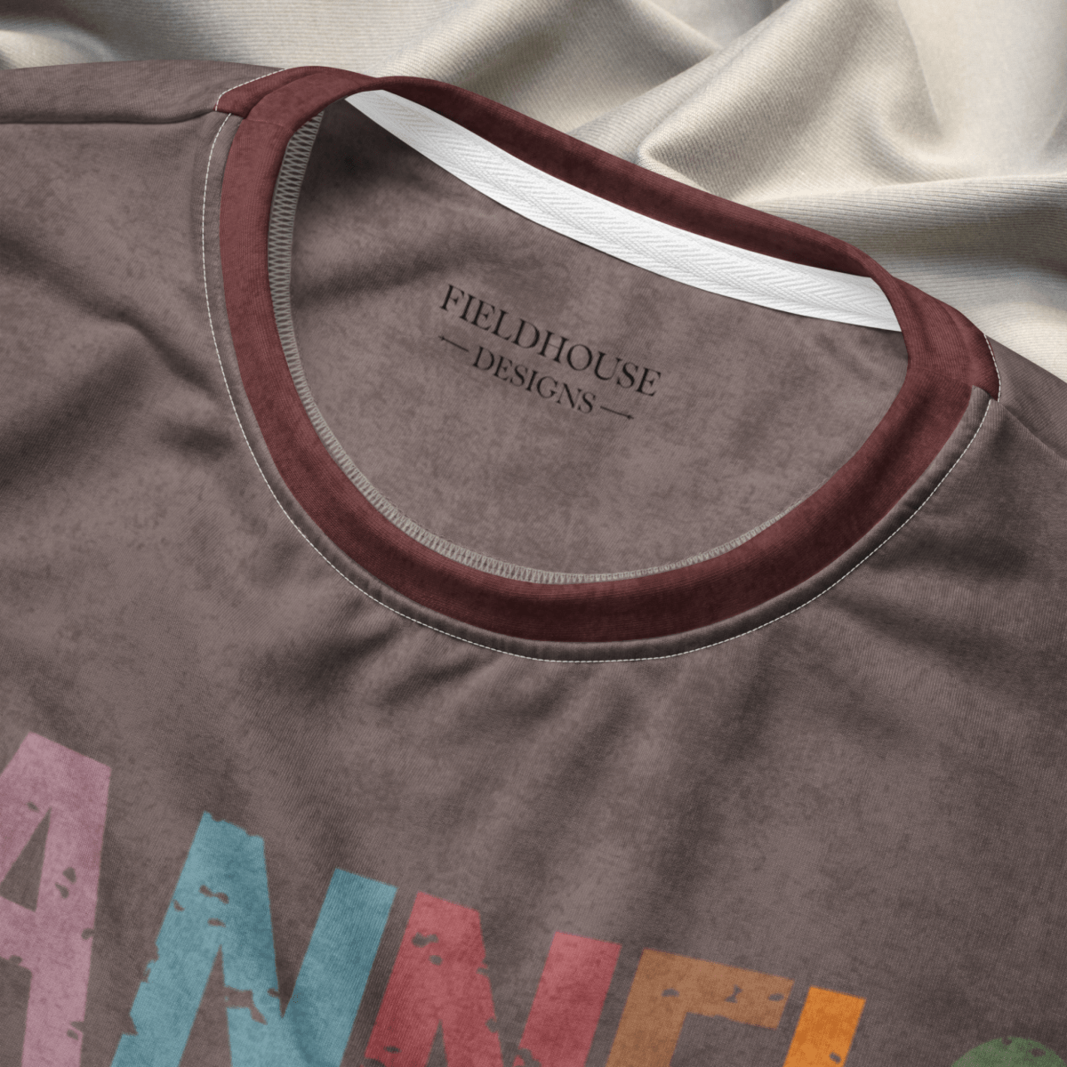Close-up of an espresso crewneck sweatshirt with 'Fieldhouse Designs' logo and colorful text on a fabric background.
