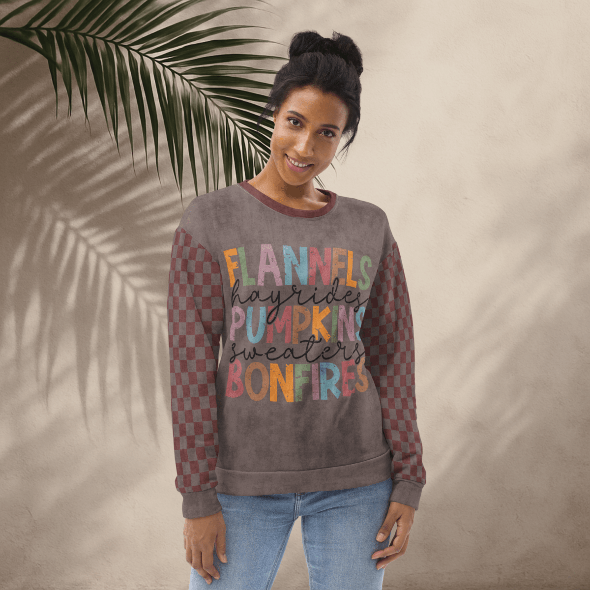 Woman wearing an espresso and burgundy sweatshirt with colorful text against a beige wall with a leafy branch.