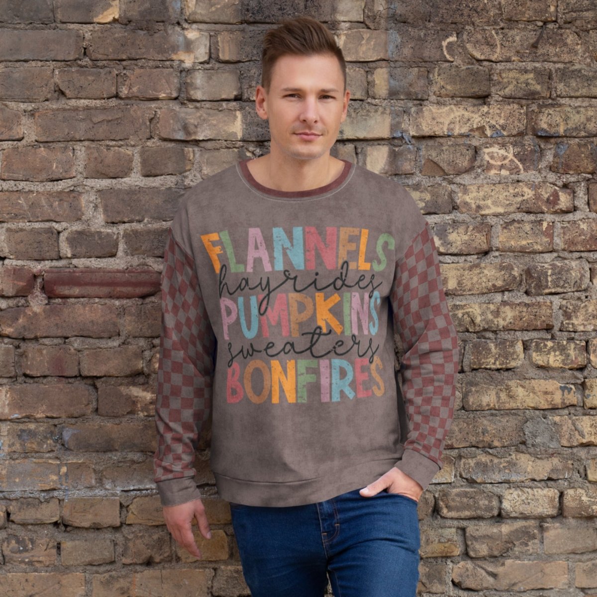 Man wearing an espresso and burgundy sweater with colorful text against a stone wall