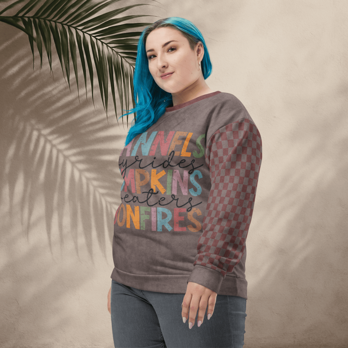 Person wearing an espresso and burgundy sweater with colorful text and pattern, standing against a beige wall with a palm leaf.