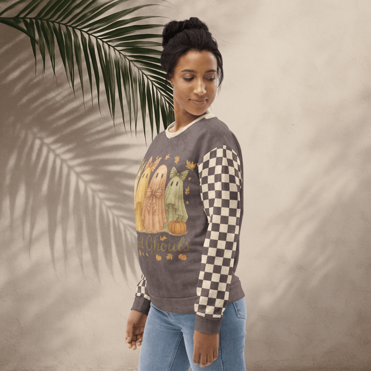 Woman wearing a sweater with a checkered pattern and graphic design, standing against a neutral background with a palm leaf.