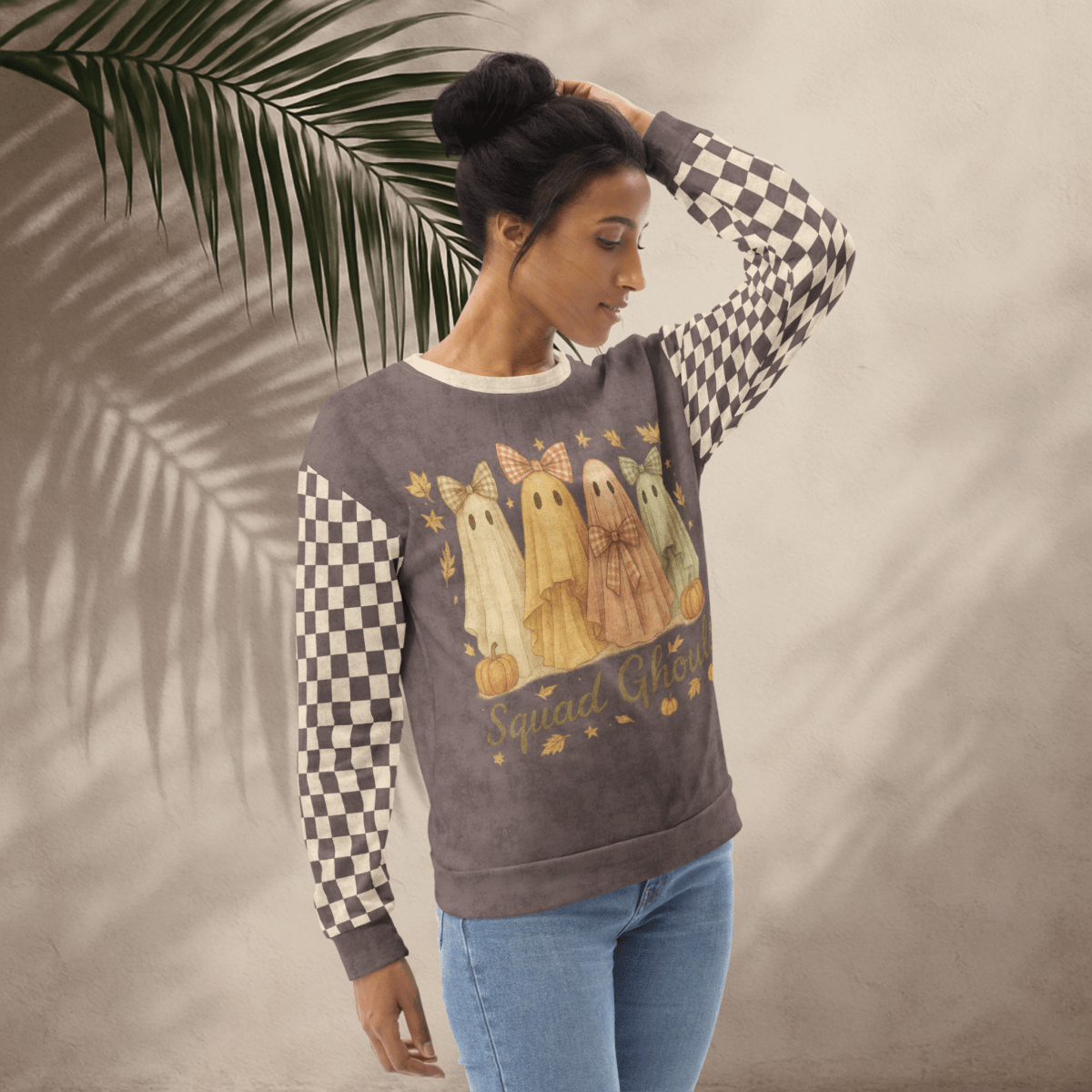 Woman wearing a sweatshirt with ghost design and checkered sleeves against a neutral background