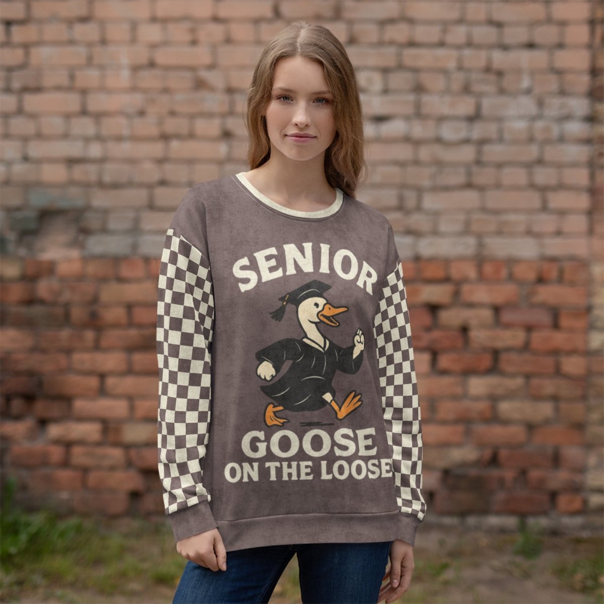 Person wearing a sweater with 'Senior Goose on the Loose' text and graphic against a brick wall.