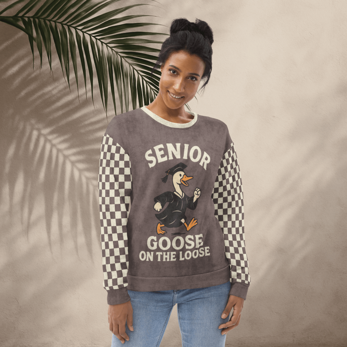 Woman wearing a sweater with 'Senior Goose on the Loose' design against a beige background