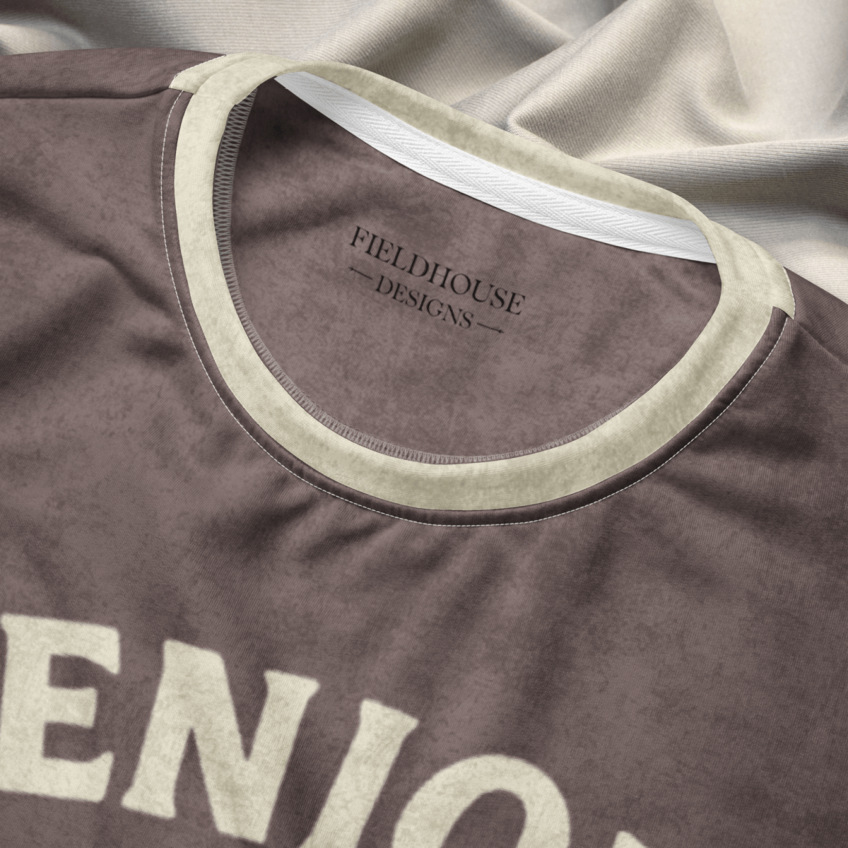 Brown shirt with 'Fieldhouse Designs' logo on a gray fabric background