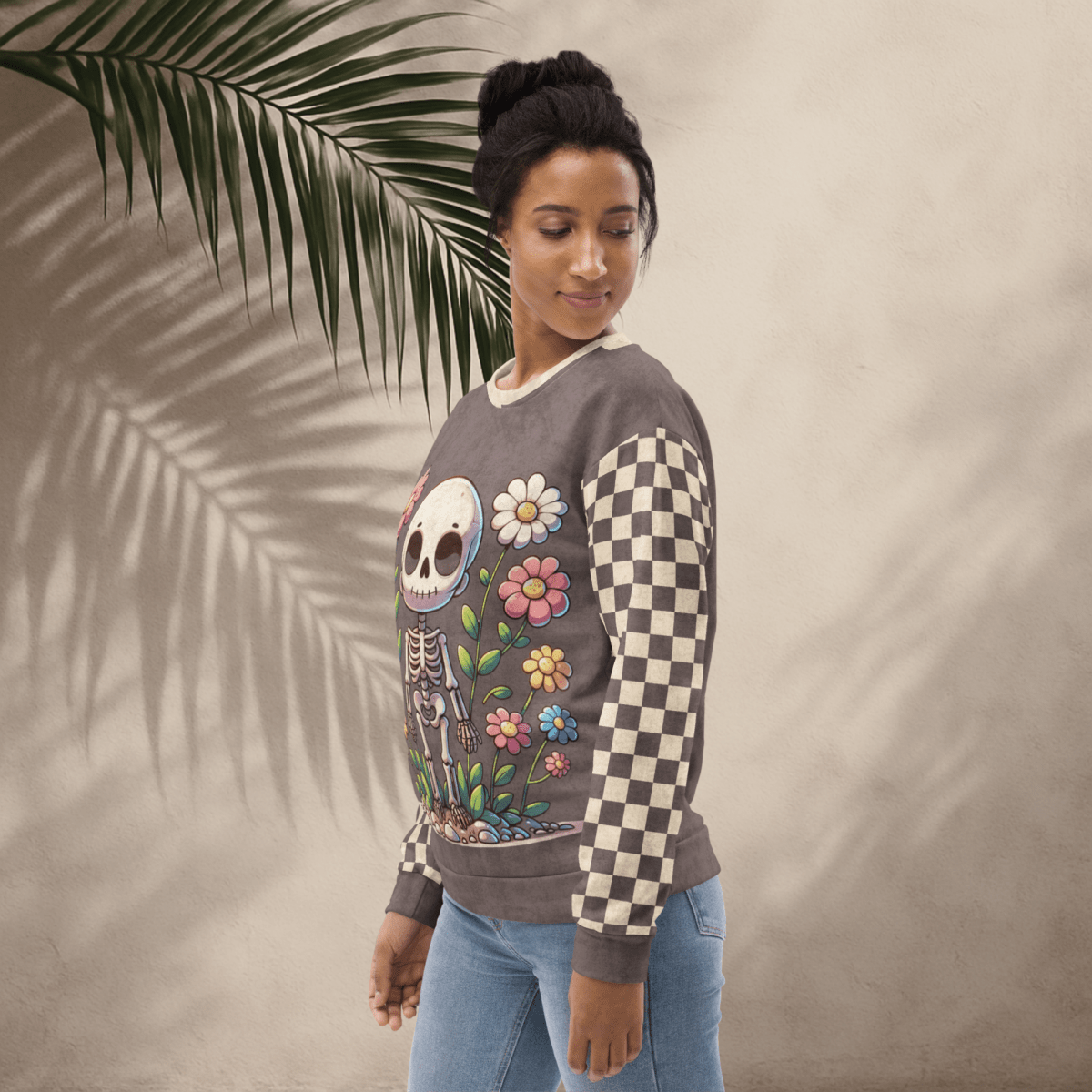 Woman wearing a sweater with a skeleton and floral design, standing against a neutral background with a palm leaf.