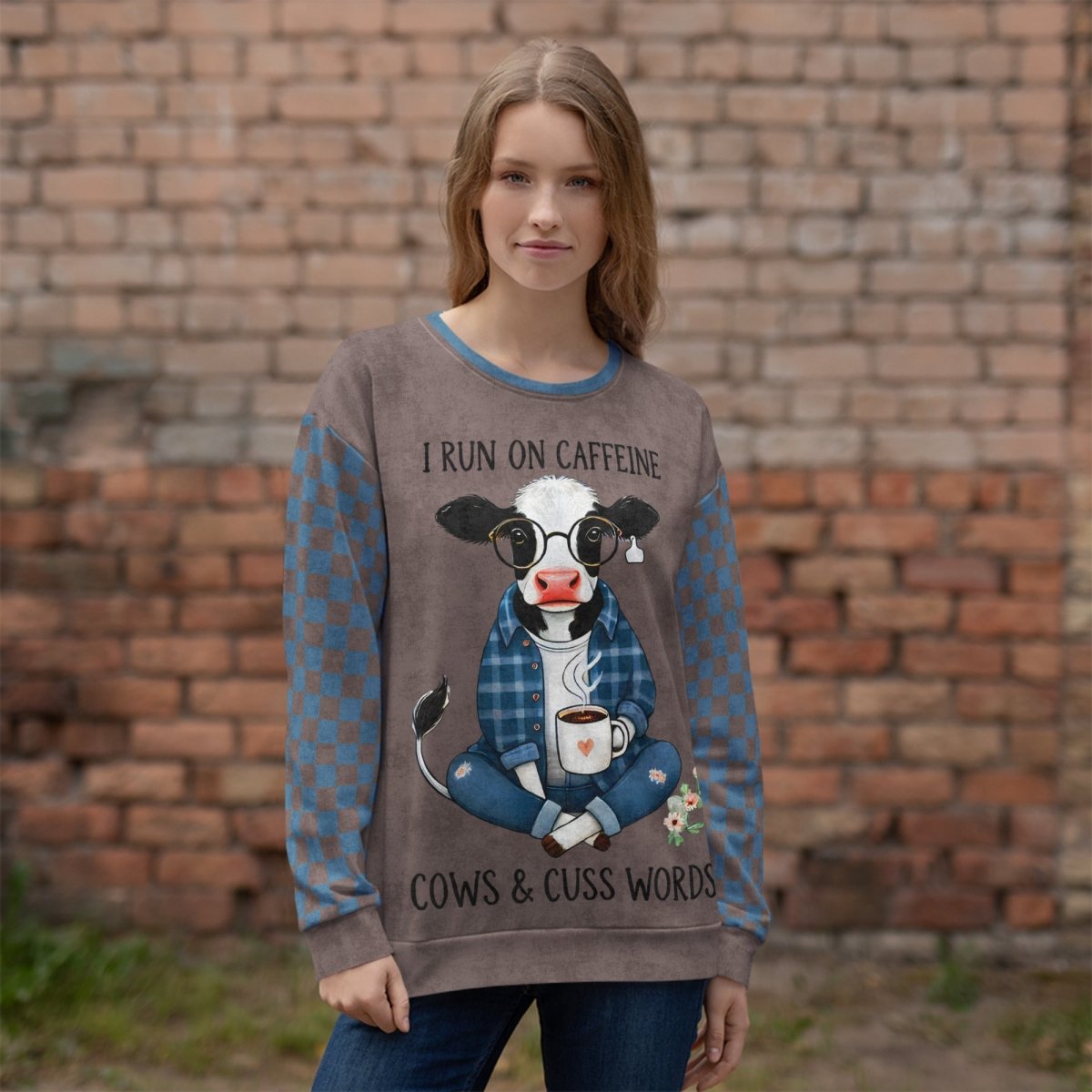 Woman wearing an Espresso and denim Sweatshirt with a cow graphic and text in front of a brick wall