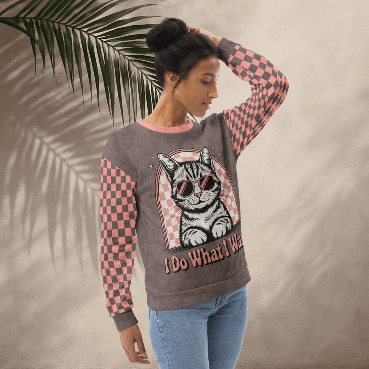model wearing Espresso sweatshirt with a sunglasses-wearing tabby cat and “I Do What I Want” text; sleeves feature pink-and-espresso checkerboard pattern with pink collar and cuffs.