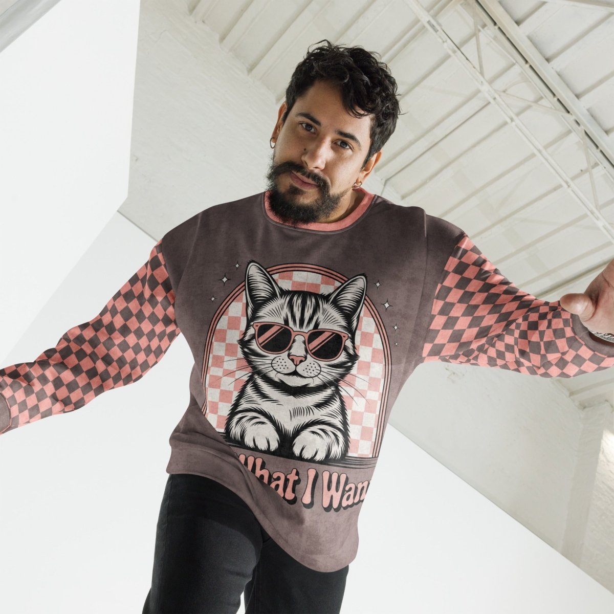 man wearing Espresso sweatshirt with a sunglasses-wearing tabby cat and “I Do What I Want” text; sleeves feature pink-and-espresso checkerboard pattern with pink collar and cuffs.