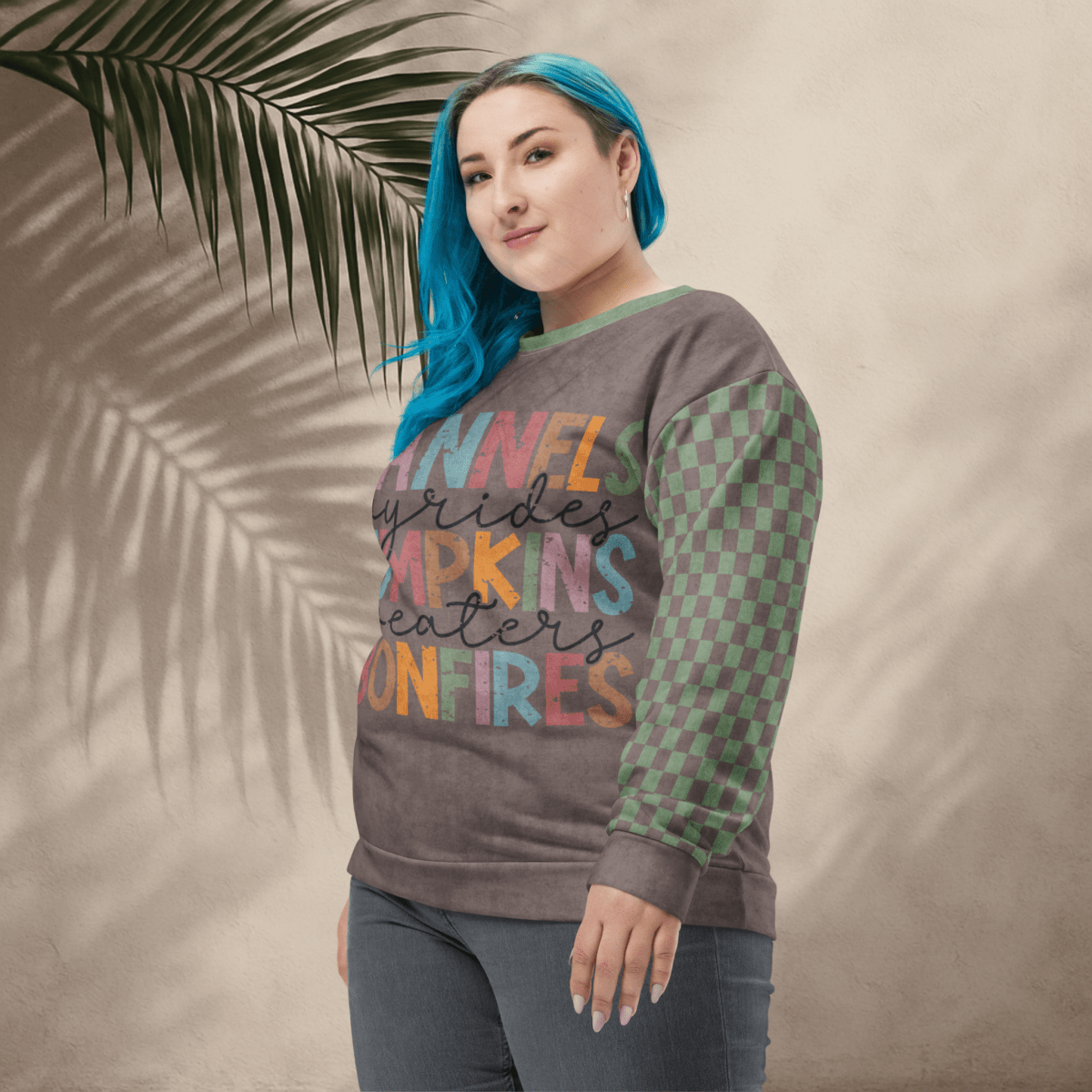Person wearing an Espresso and sage green colorful sweatshirt with text and pattern, standing against a beige wall with a palm leaf.