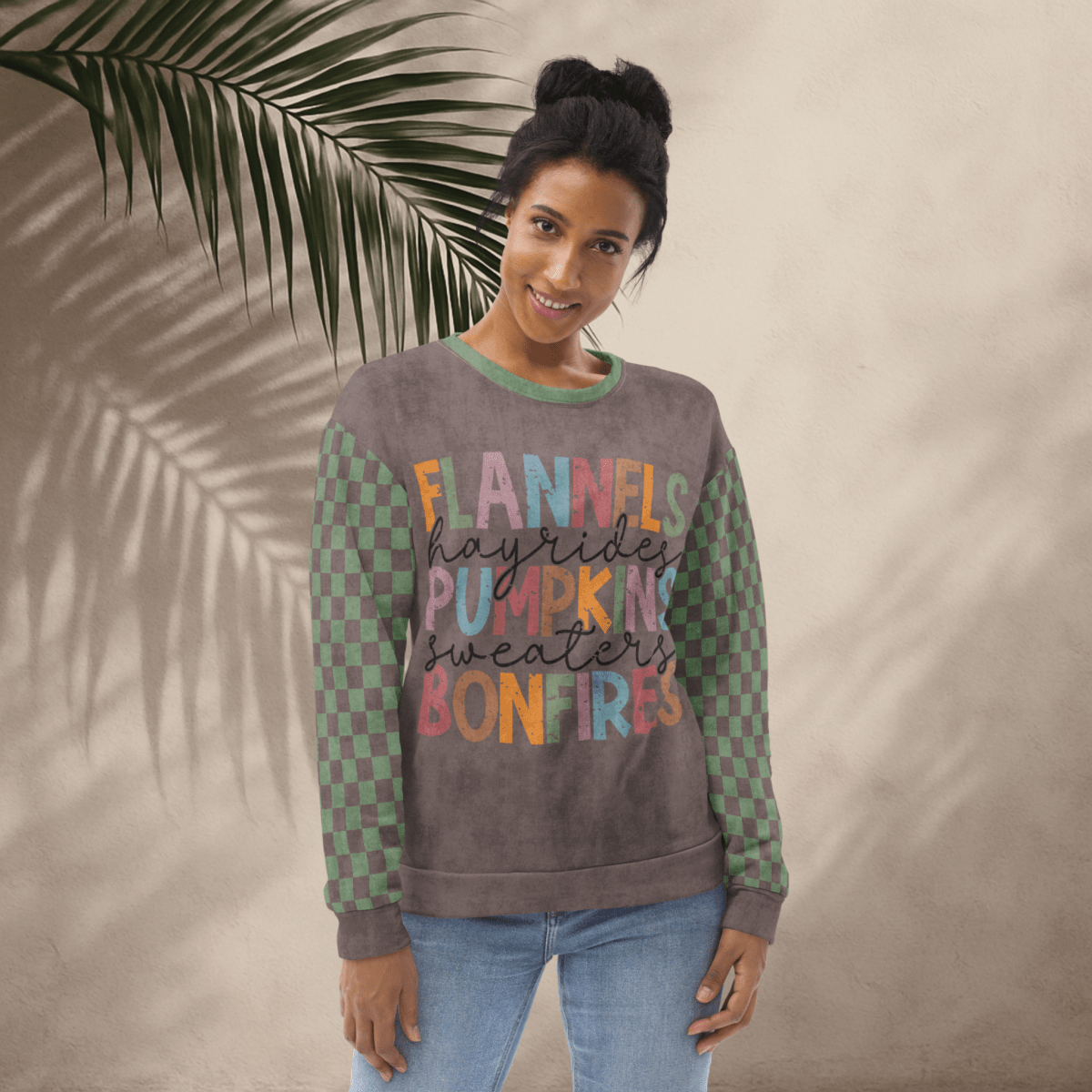 Woman wearing an Espresso and sage green sweater with colorful text against a beige wall with a leafy branch.
