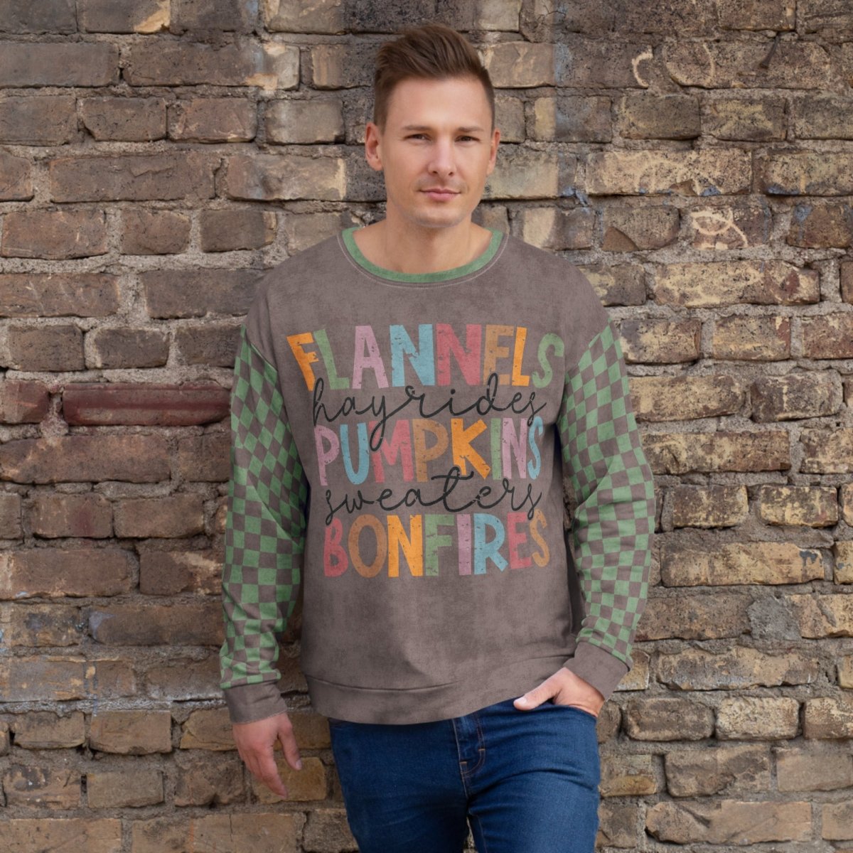 Man wearing an Espresso and sage green sweater with colorful text against a stone wall