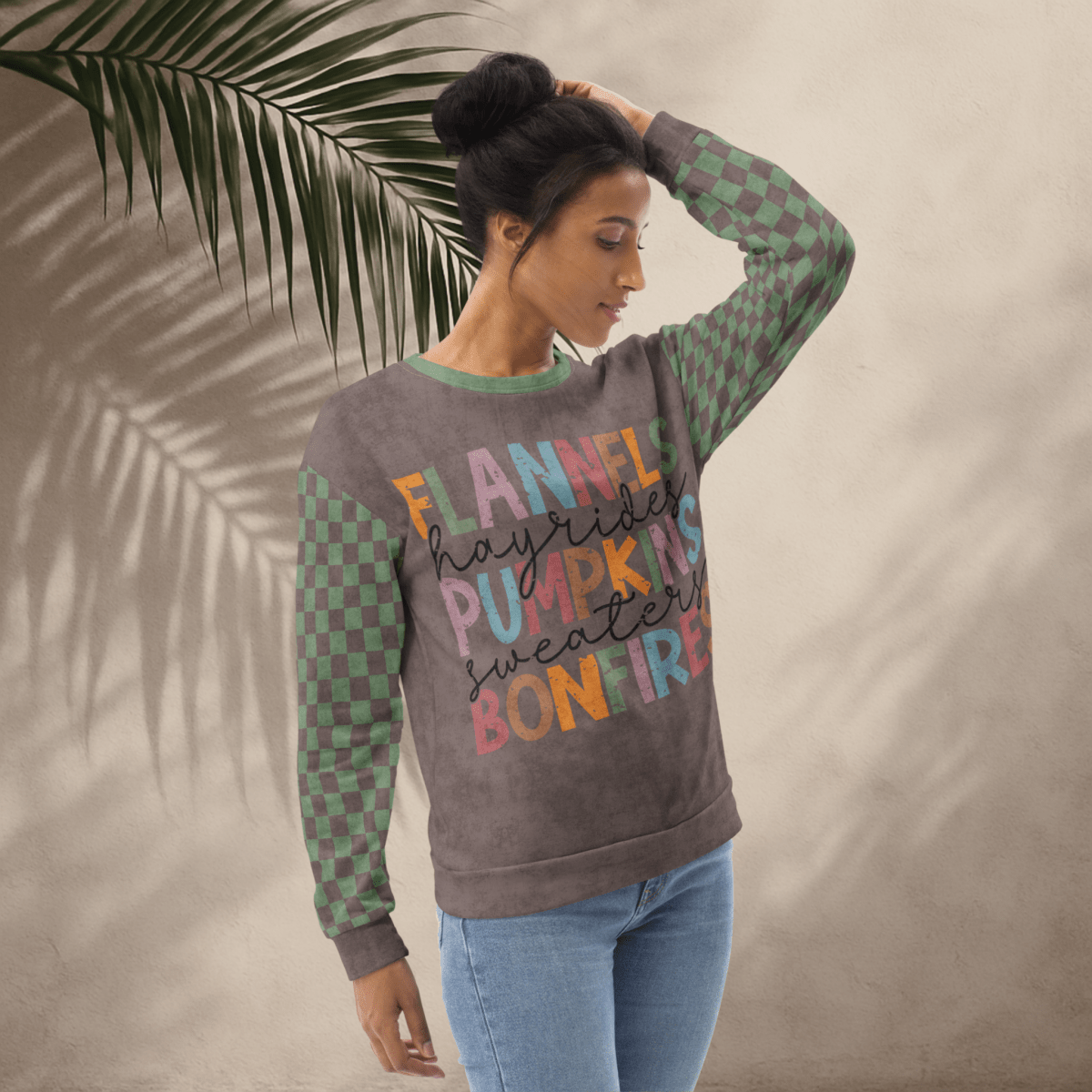 Woman wearing an Espresso and sage green colorful text sweater with a leafy background