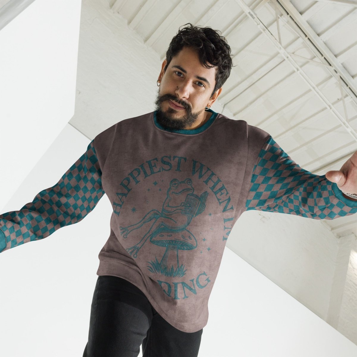 Man wearing an espresso and teal sweater with Frog reading with "Happiest When I'm Reading" text design, standing indoors.